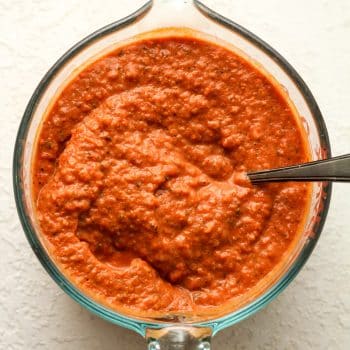 A measuring cup of vodka pizza sauce with a spoon.