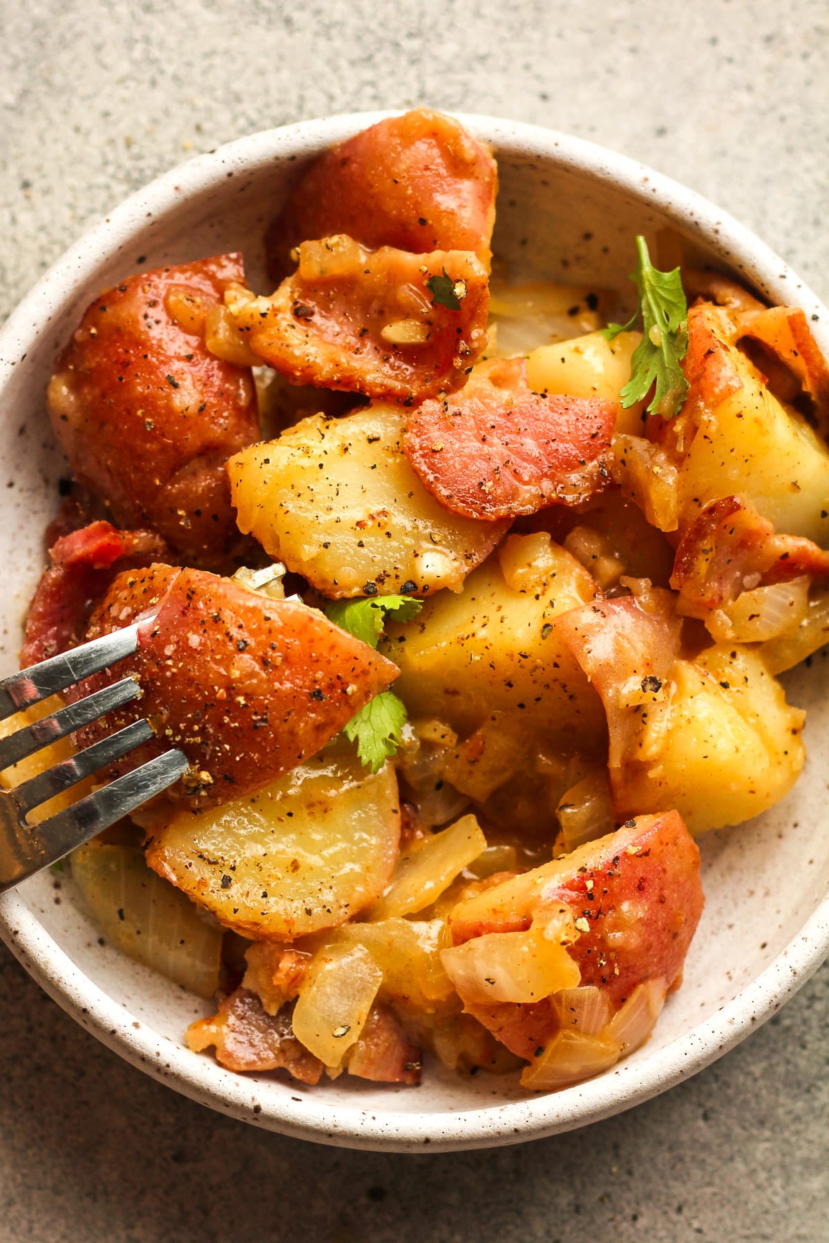 A serving of German potato salad with a fork stabbing a potato chunk.