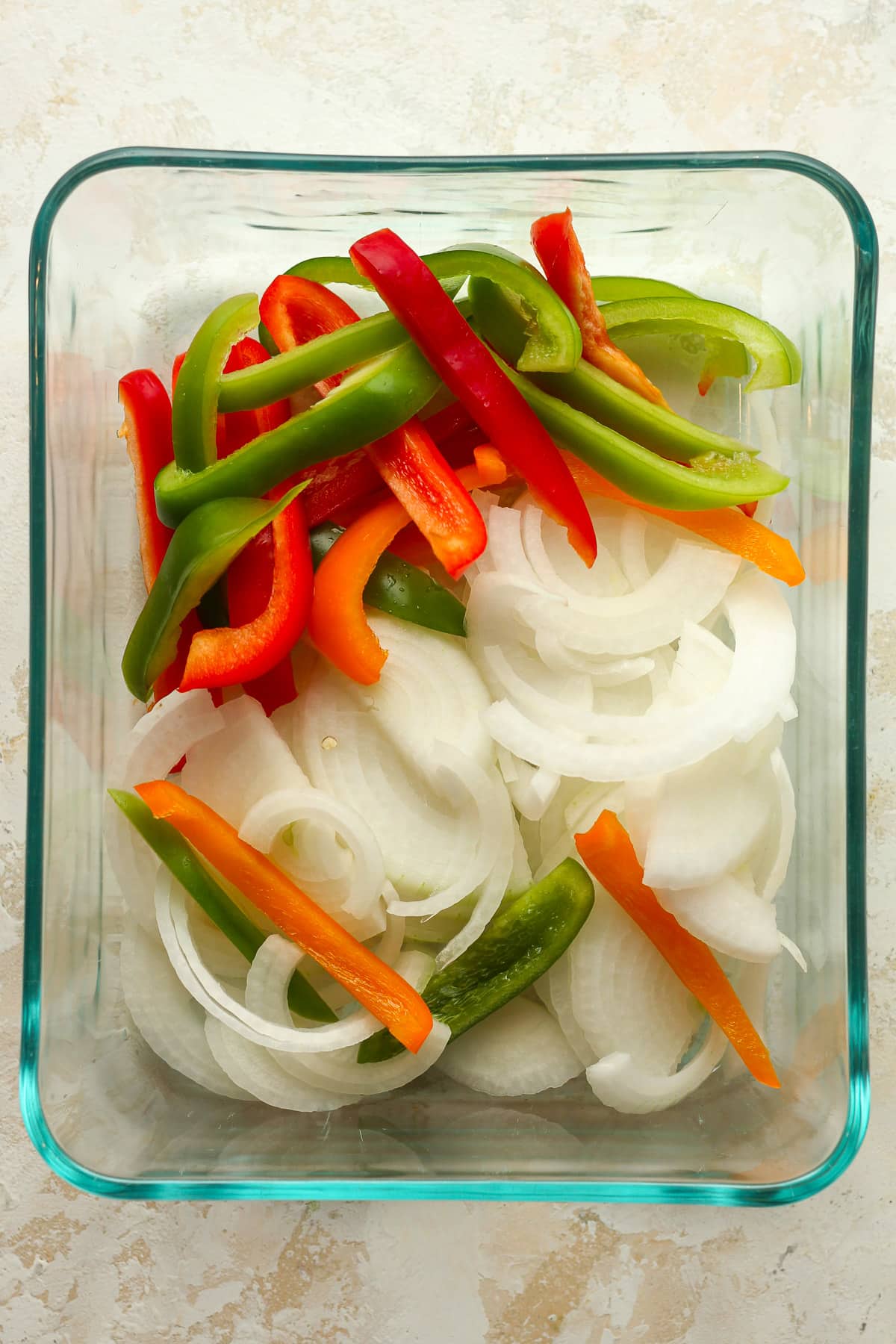 A rectangular glass dish with sliced onion and bell peppers.