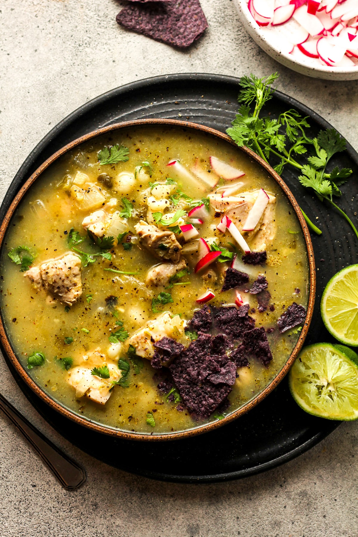 A bowl of chicken pozole verde with garnishes on top.
