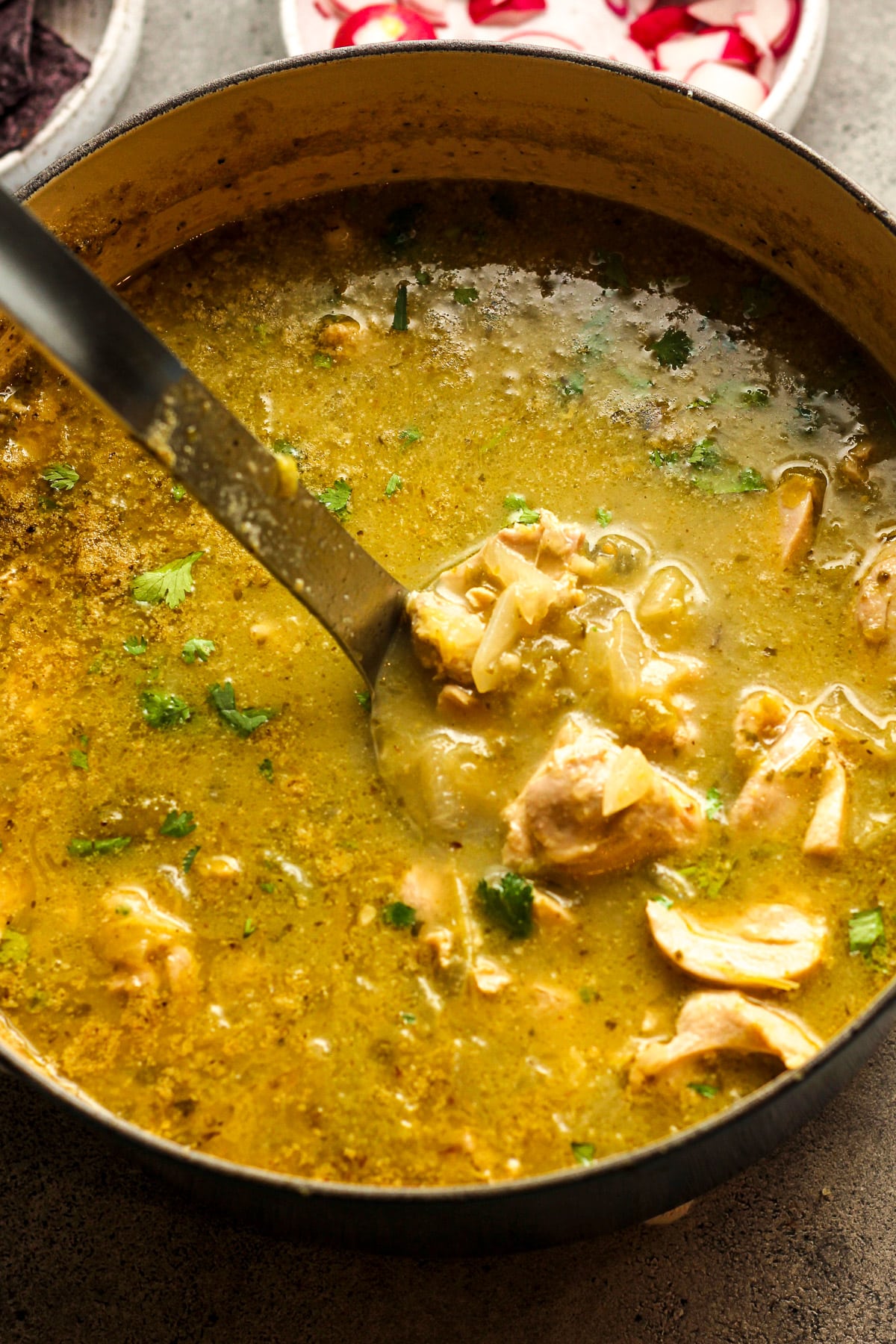 A large stock pot of chicken pozole verde with a soup ladle inside.