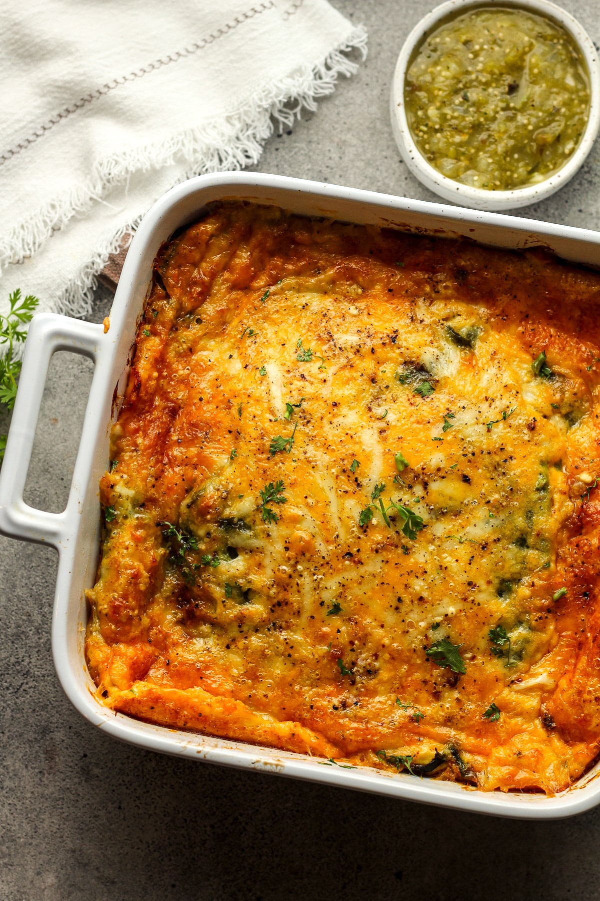 Overhead view of a chile relleno casserole with a small bowl of salsa verde.