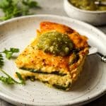 Side view of a slice of chile relleno casserole with a dollop of salsa verde.