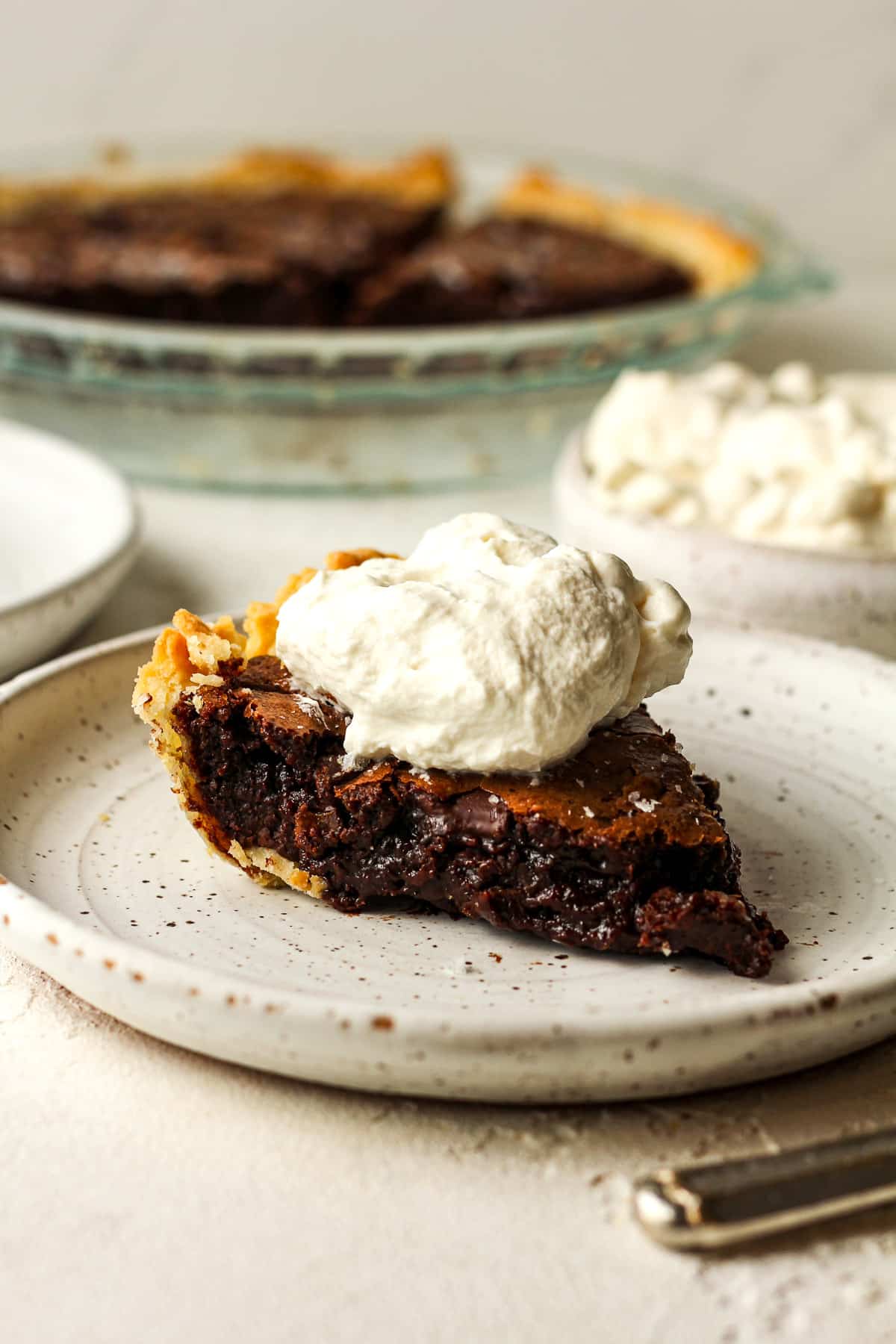 Side view of a slice of triple chocolate brownie pie with whipped cream on top.