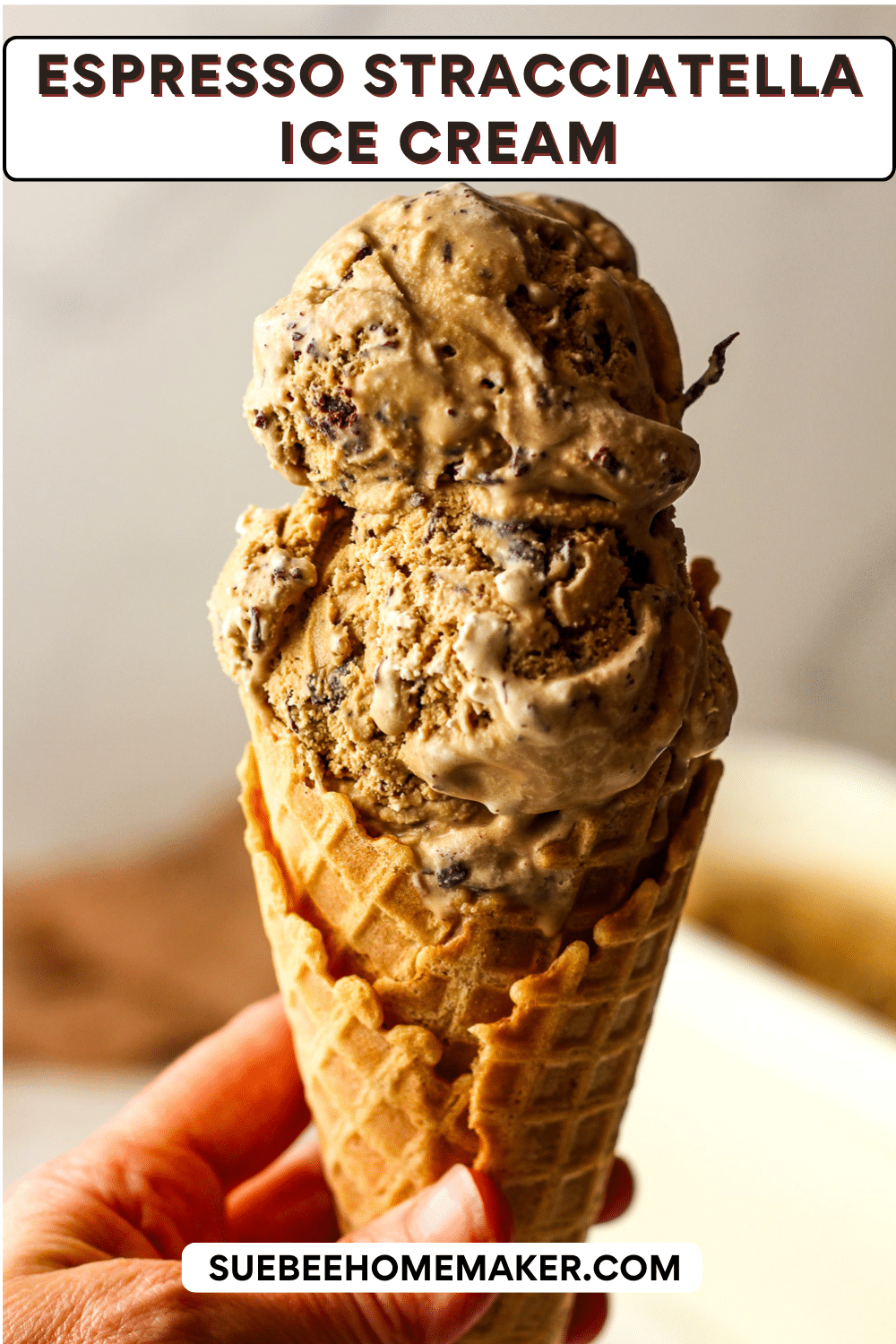 My hand holding a waffle cone with espresso stracciatella ice cream.