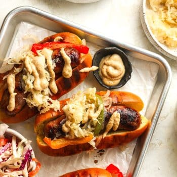 Closeup on some grilled beer brats in buns with topings.
