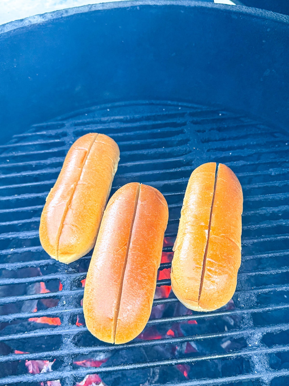Three grilled hotdog buns on the grates.
