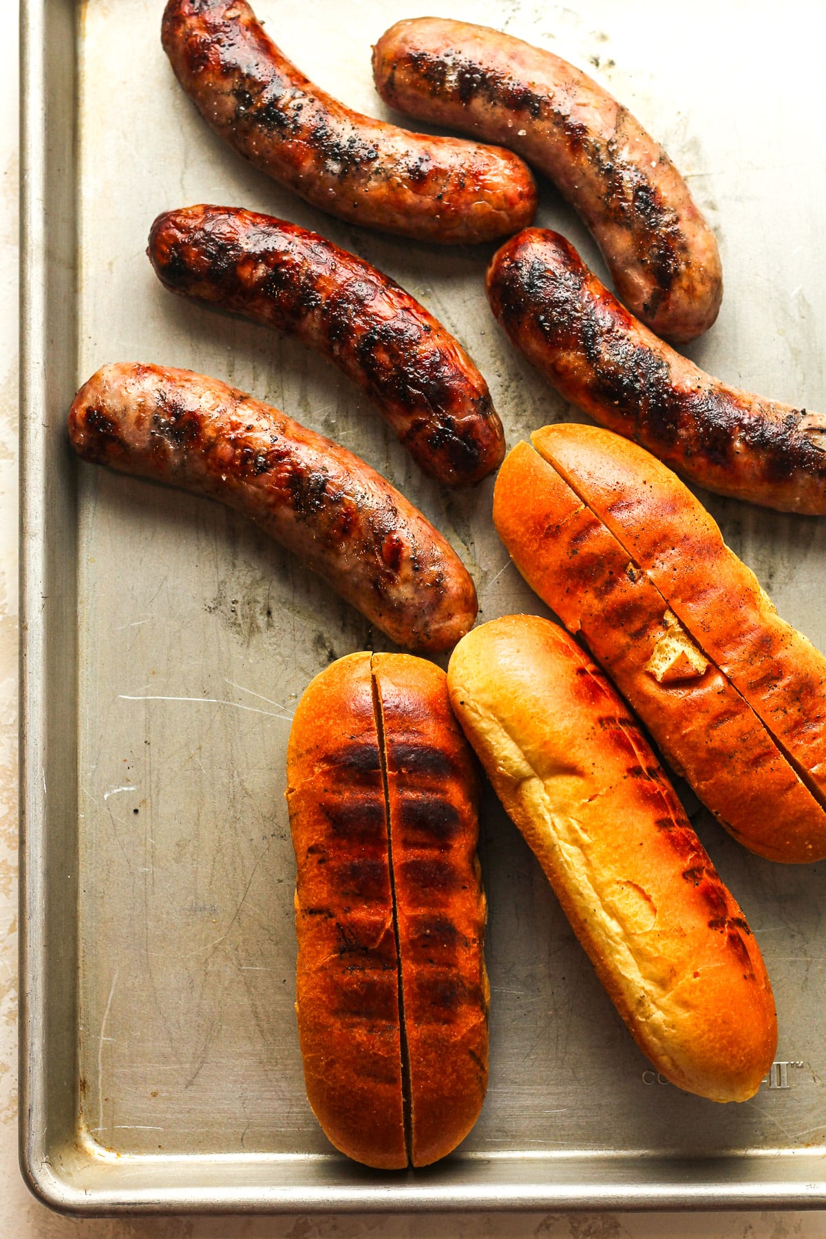 A pan of the charred brats and toasted buns.