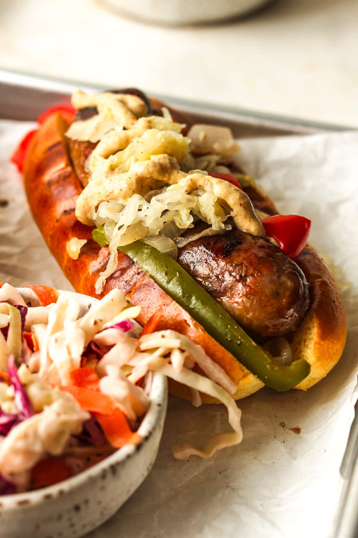 Side view of a grilled beer brat with toppings in a pan.