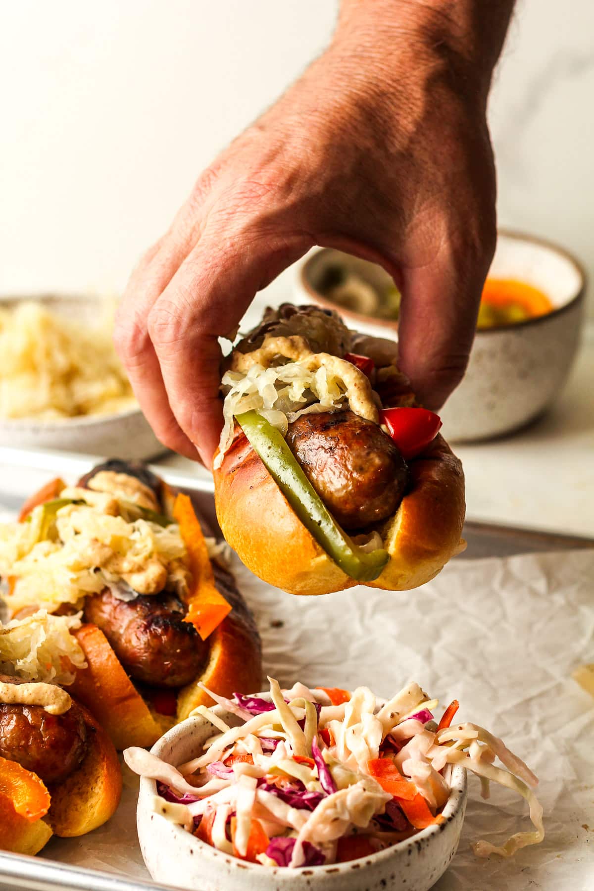 A hand holding a grilled beer brat with peppers, onions, and sauerkraut.