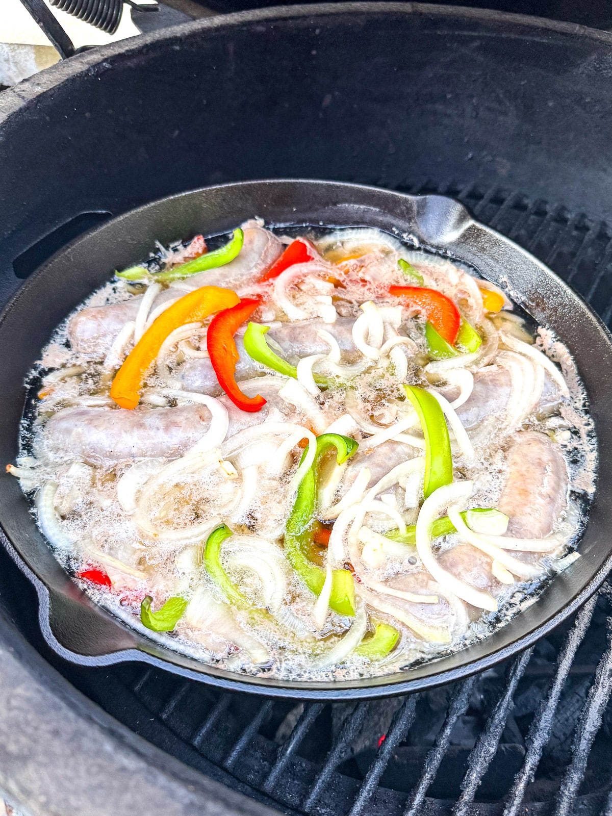 A cast iron skillet with the brats mixture boiling over the fire.