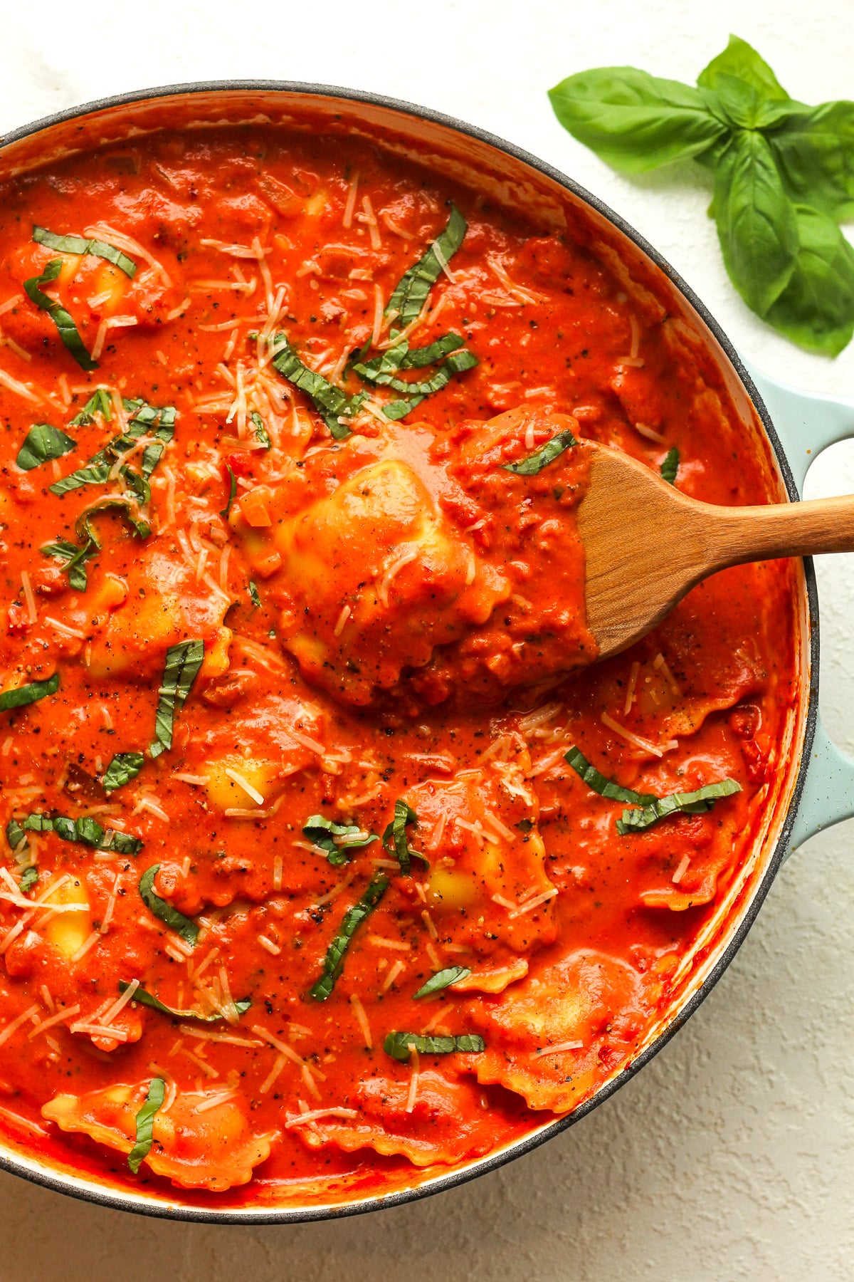 A shallow braiser with ravioli alla vodka showing a wooden spoon lifting some up.