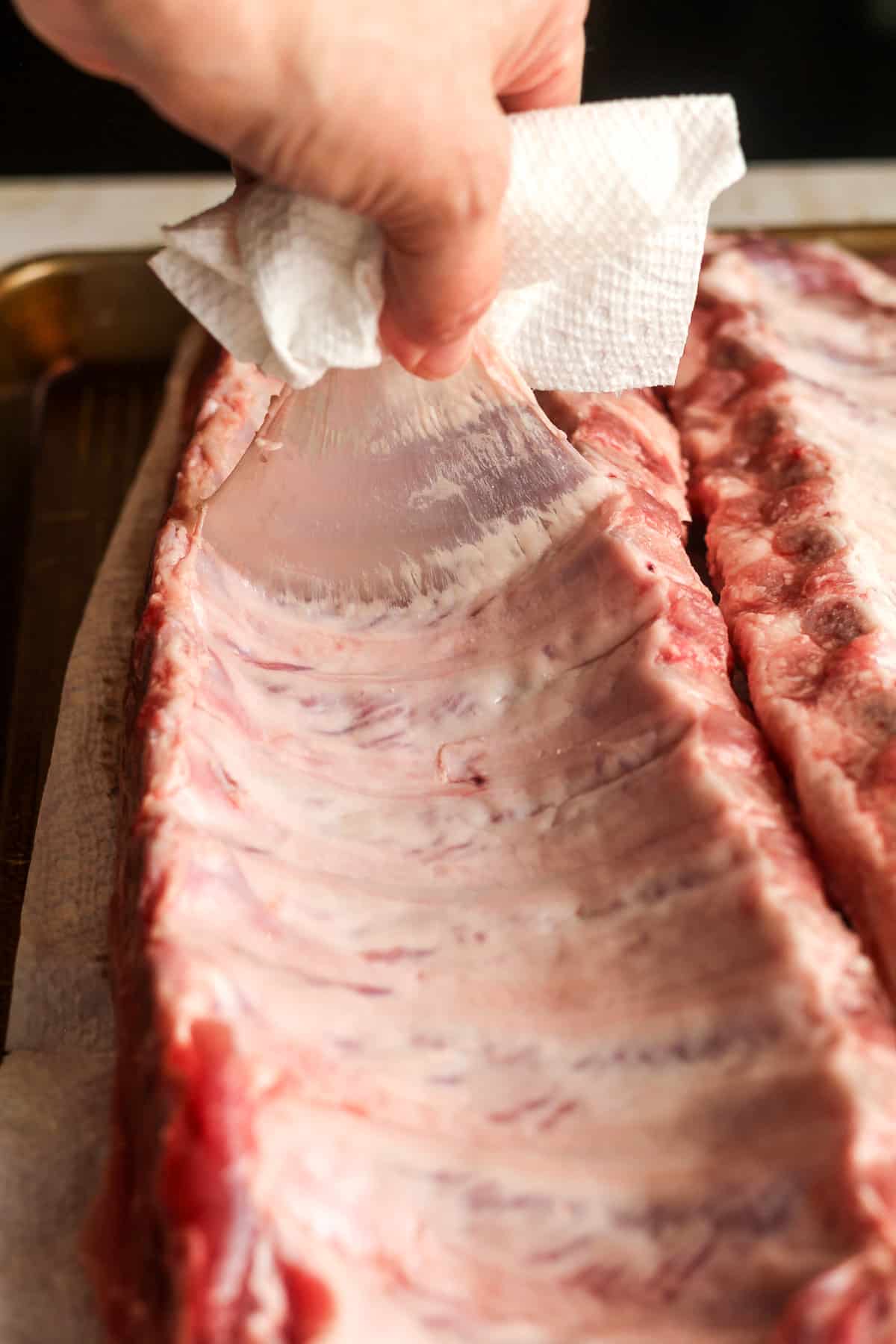My hand using a napkin to pull the membrane off the bottom of the rack of ribs.