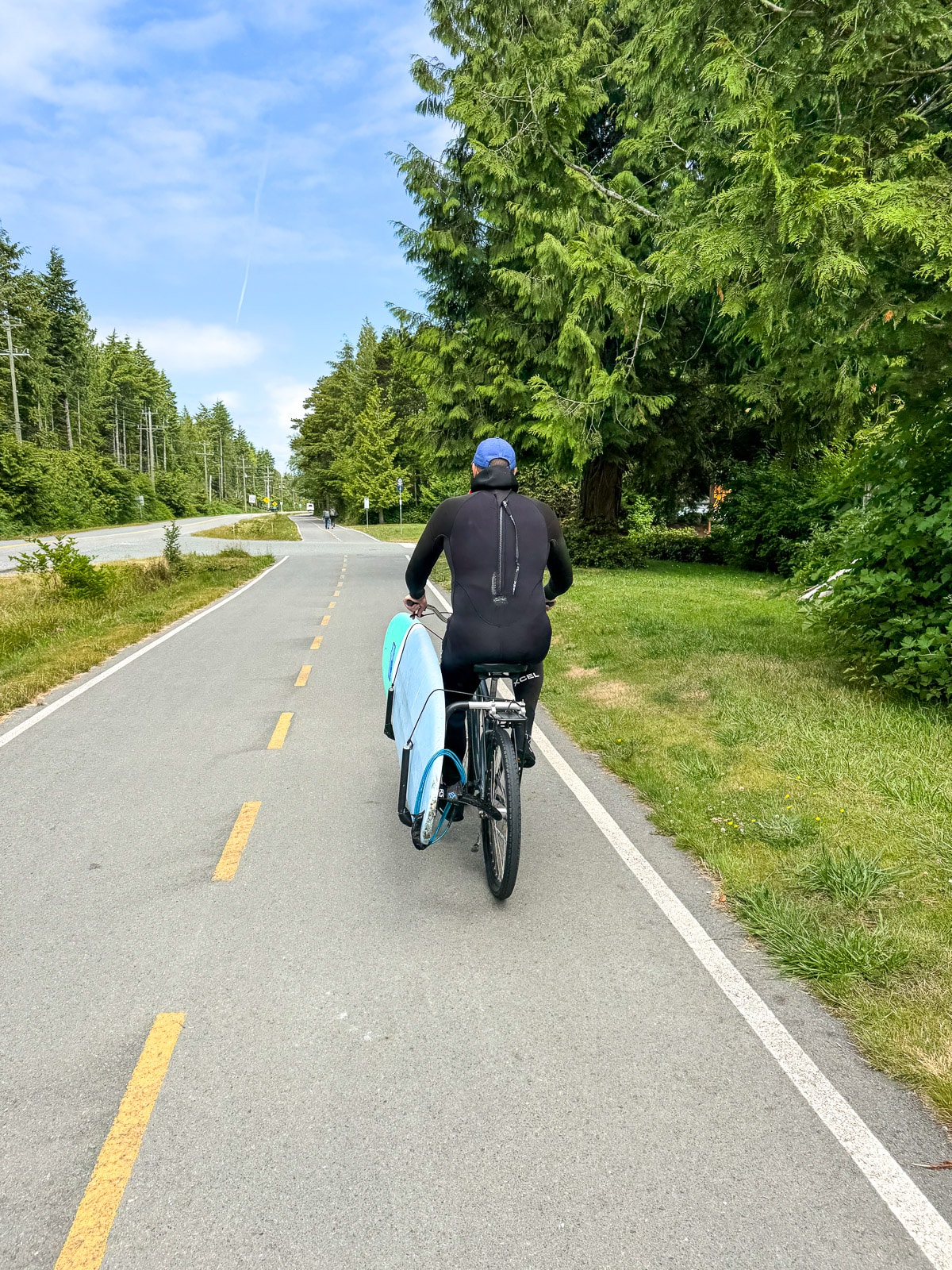 Mike riding a bike with in wetsuit with the surfboard attached to bike.