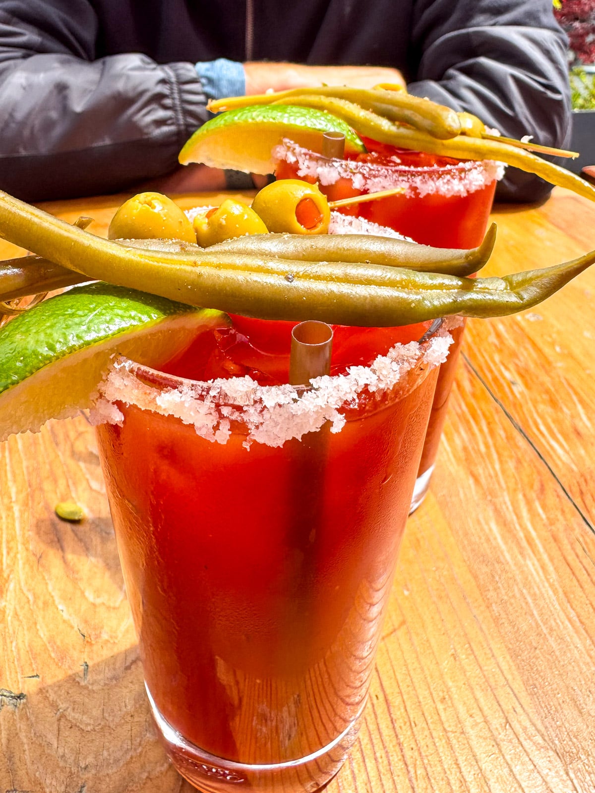 Side view of two bloody marys with olives and green beans.