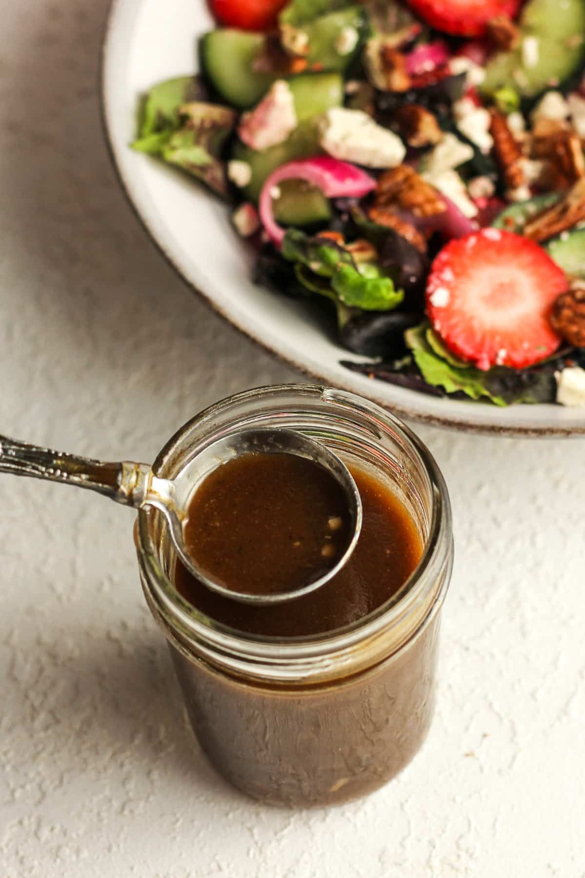 A jar of balsamic dressing with a tablespoon on top.