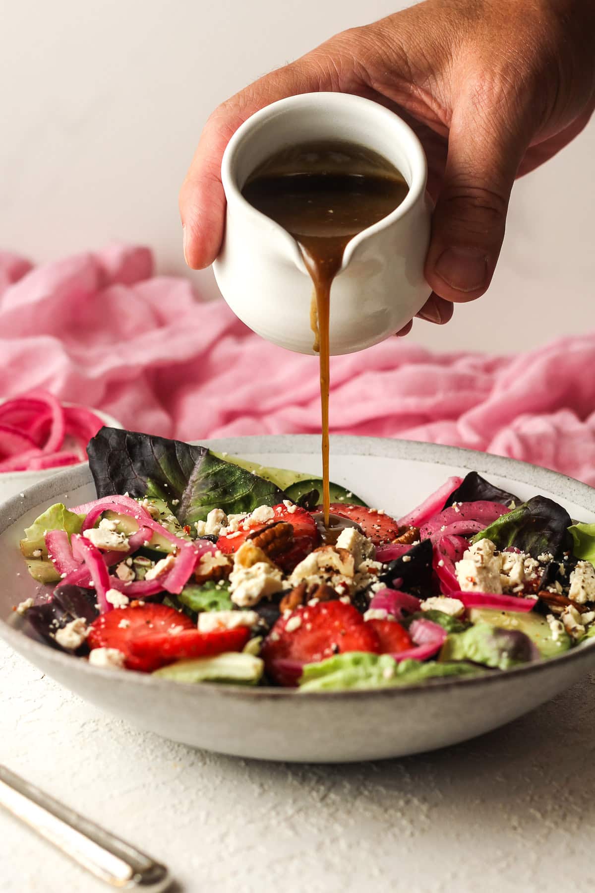 A hand pouring the balsamic dressing over the salad.