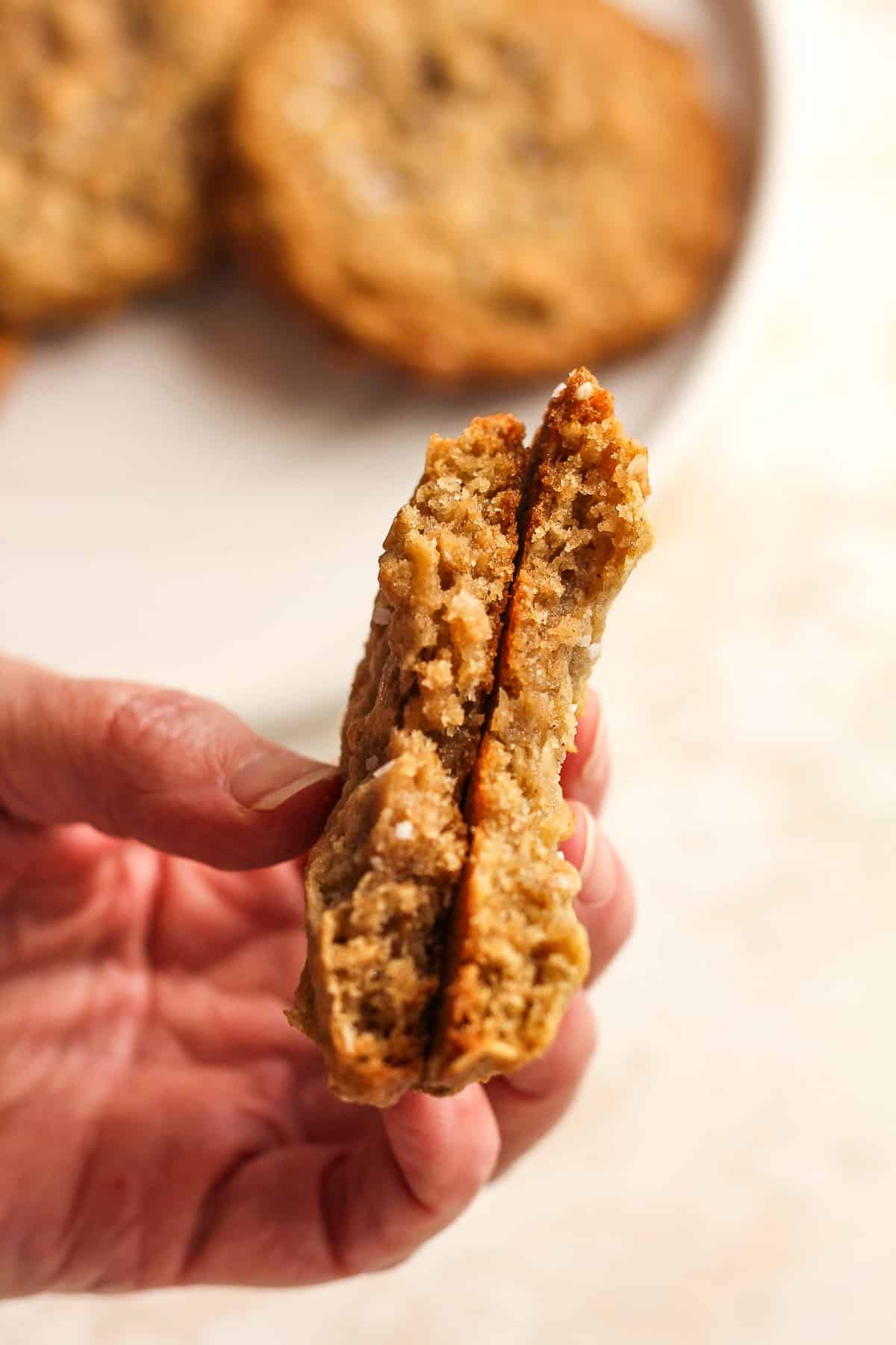 A hand holding a halved brown butter oatmeal cookie.