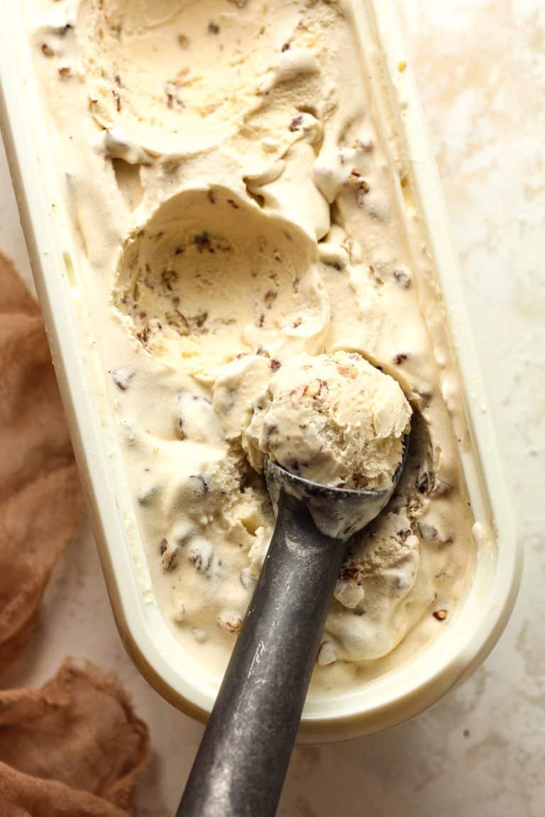 An ice cream scoop of butter pecan ice cream in a white container.