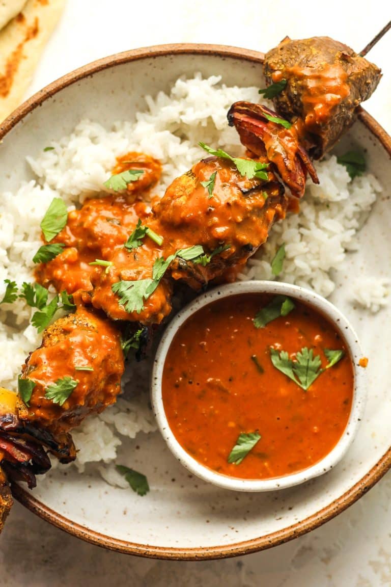 A butter chicken skewer over rice, with a small bowl of sauce.