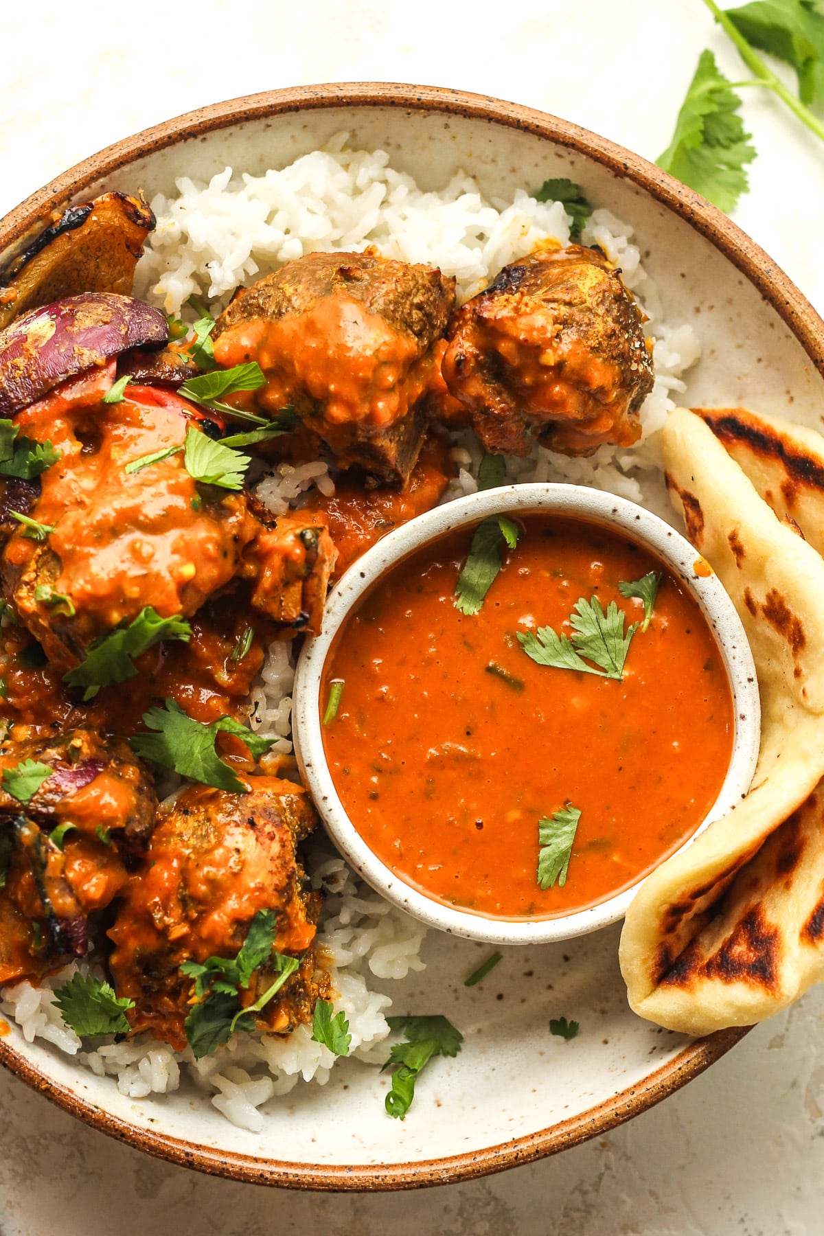 Closeup on a bowl of the butter chicken kabobs with a small bowl of sauce and a piece of naan bread.
