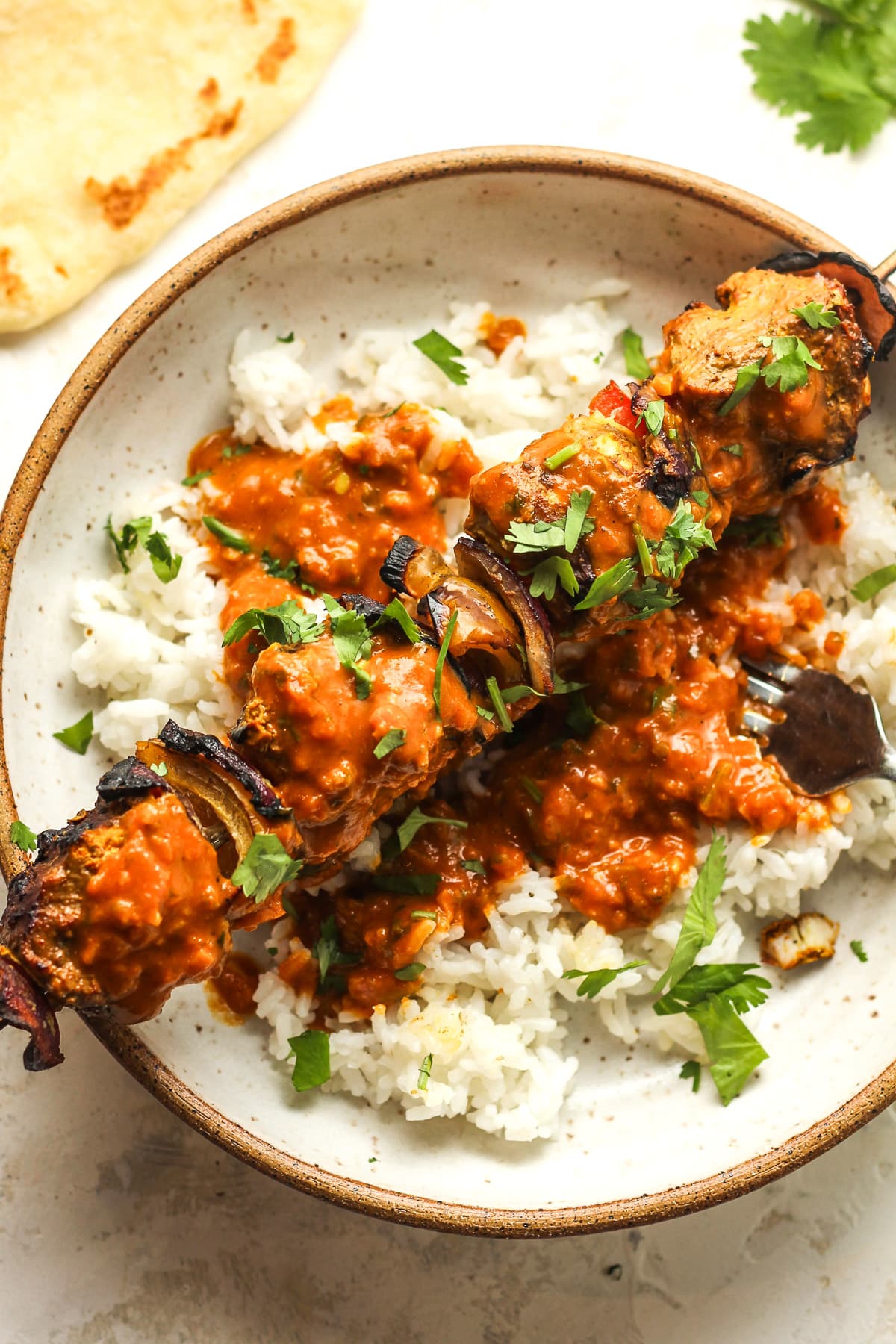 A bowl with rice, one kabob, and some butter chicken sauce on top.