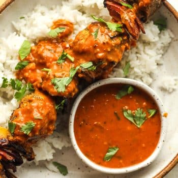 Closeup on a butter chicken kabob over rice with butter sauce on the side.