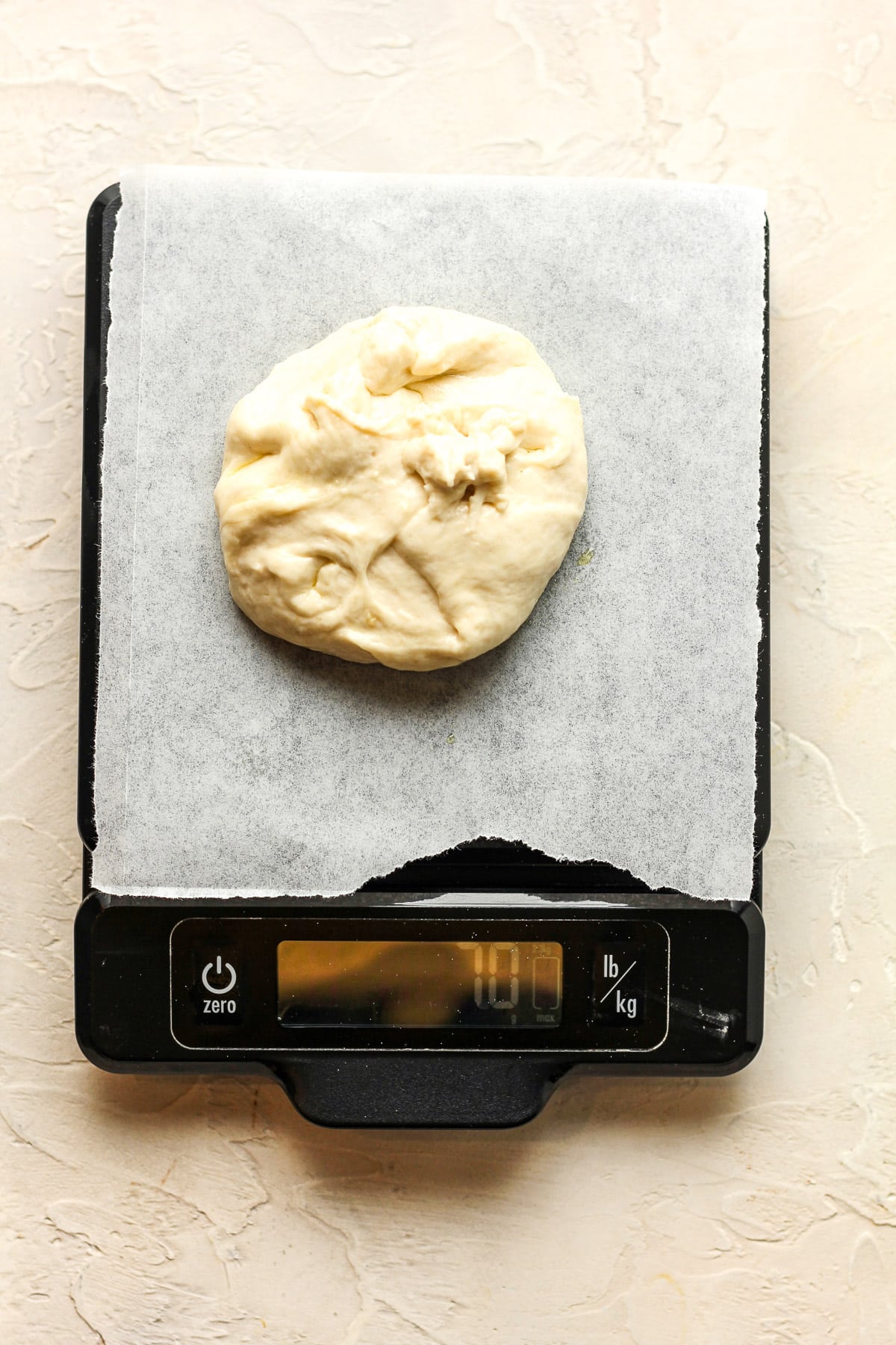 A digital scale with a square of parchment paper with a round of dough.