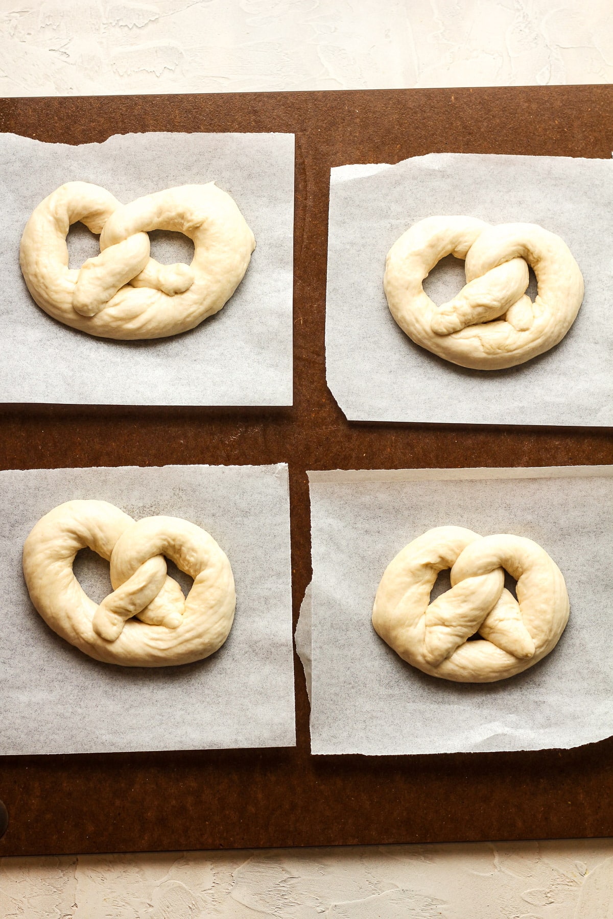 The formed pretzels on little pieces of parchment paper on a large board.