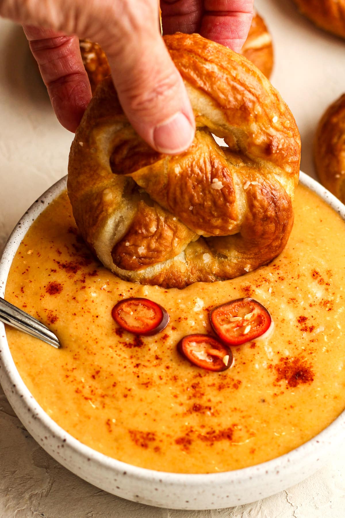A closeup of a hand dipping a soft prezel into a bowl of spicy beer cheese dip.