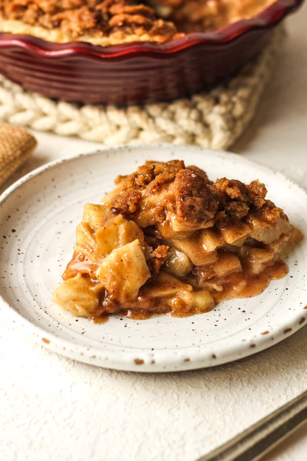 A plate with a slice of pie with the remaining pie in the background.