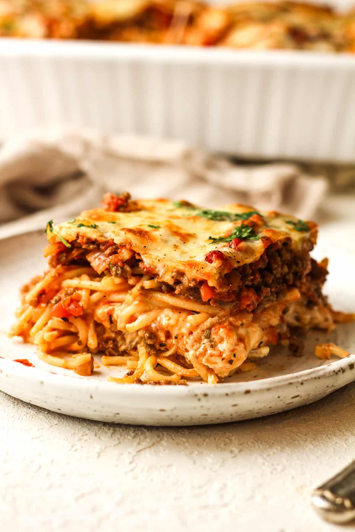 Side view of a slice of millionaire spaghetti casserole with the casserole in the background.