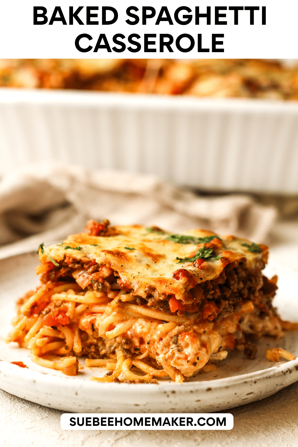 Side view of a square of baked spaghetti casserole with the remaining casserole in the background.