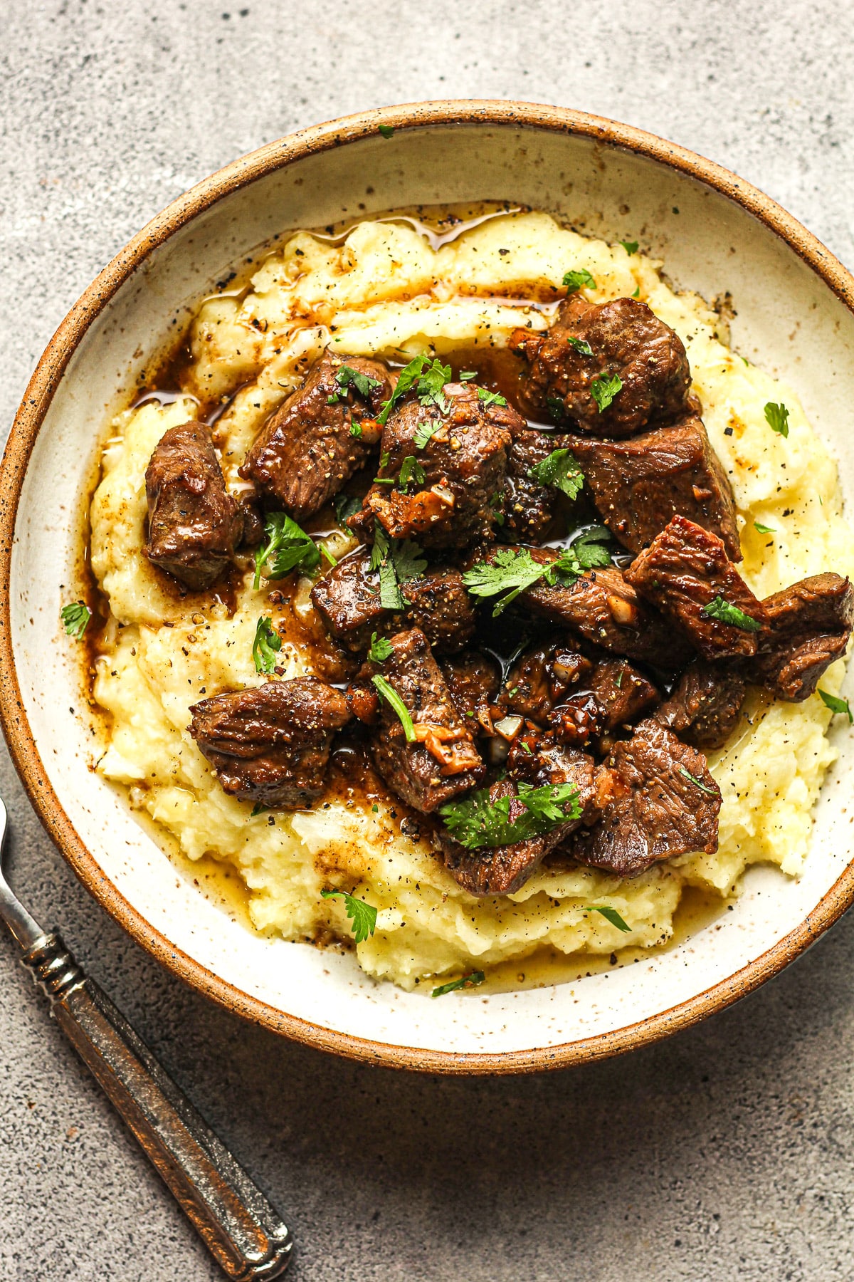 A bowl of garlic butter steak bites over cauliflower potato mash.