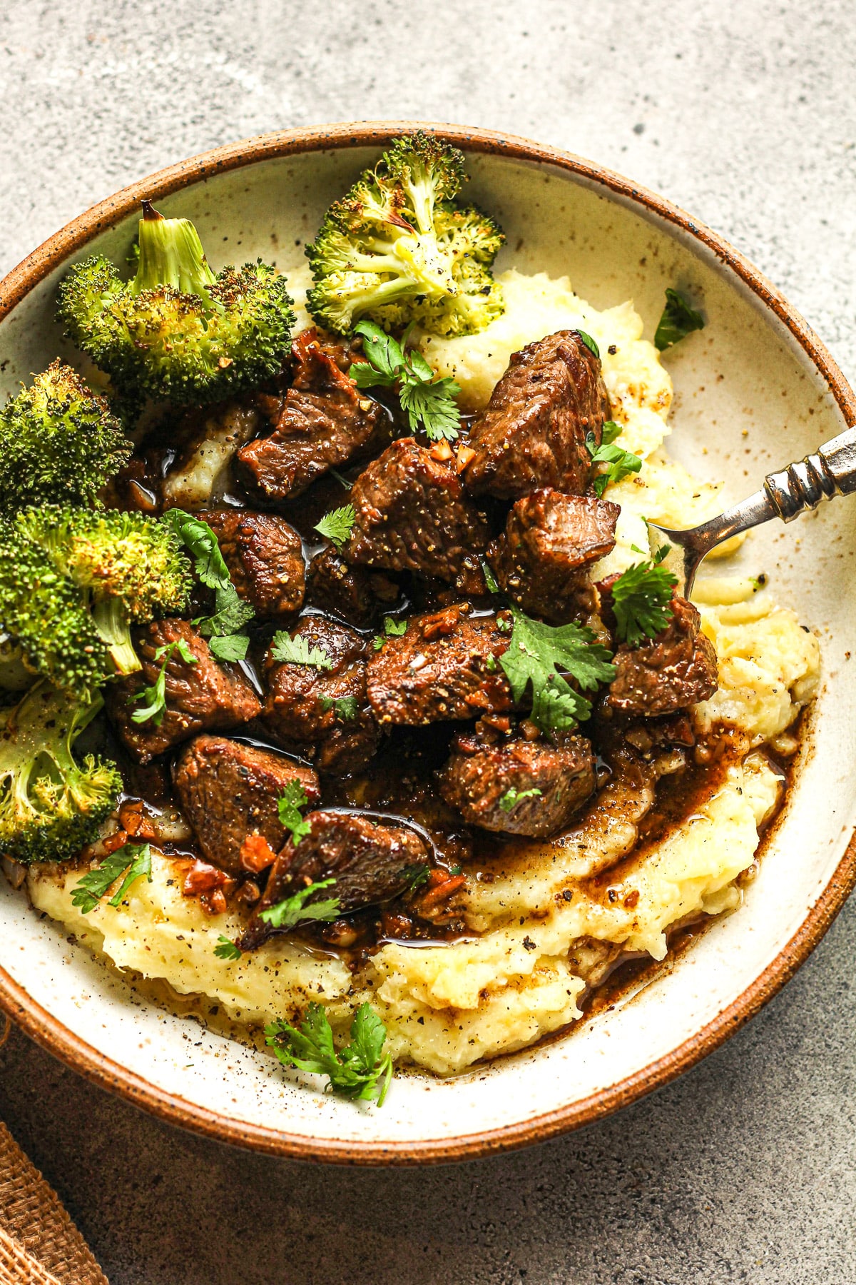 A bowl of steak bites over cauliflower potato mash with roasted broccoli.