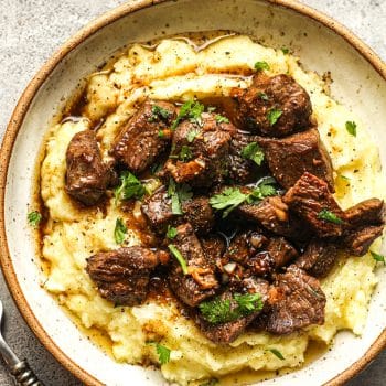 Closeup on a bowl with crispy steak bites over cauliflower potato mash.