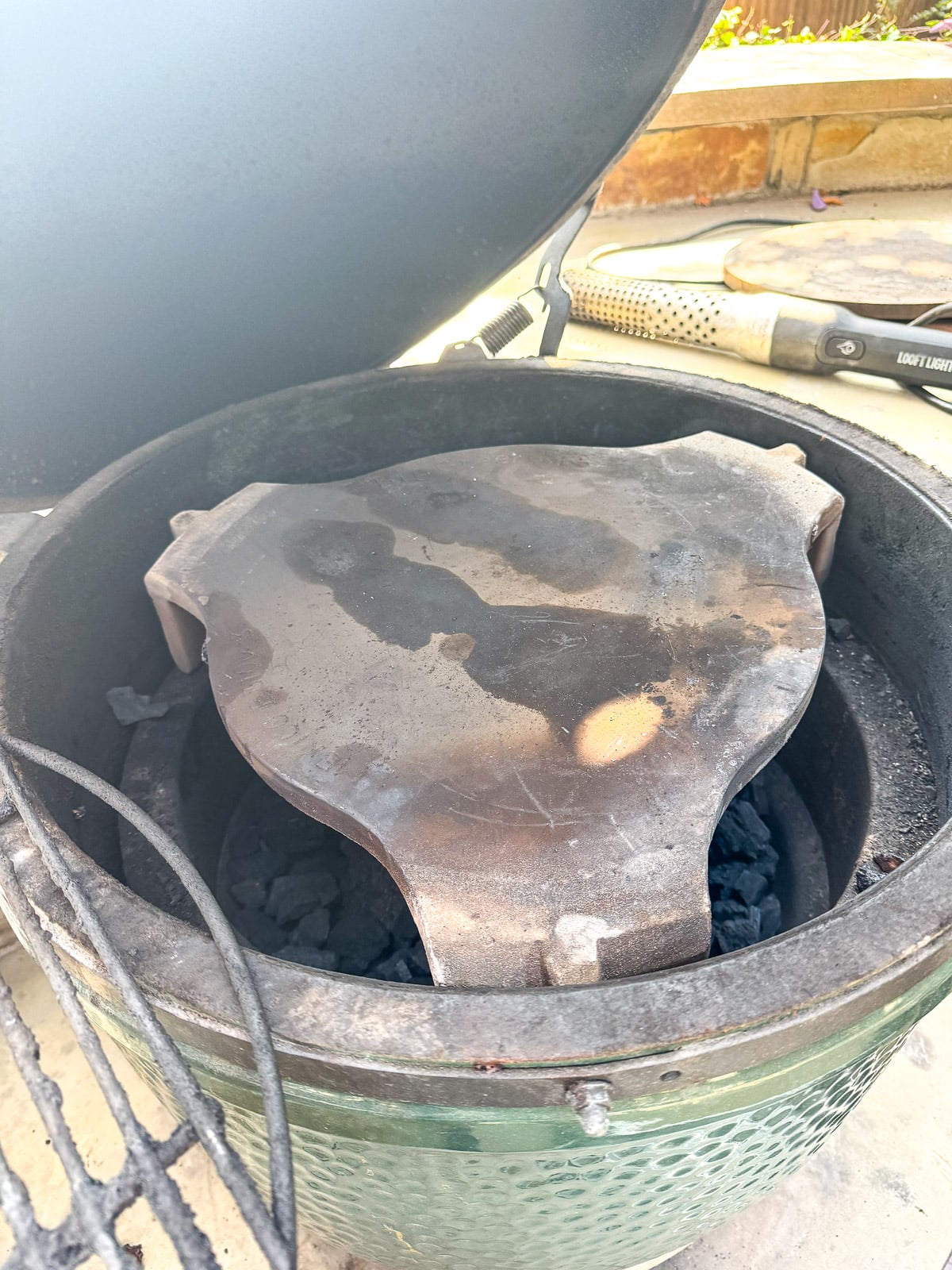 The Big Green Egg showing the convEGGtor with a stone on top.