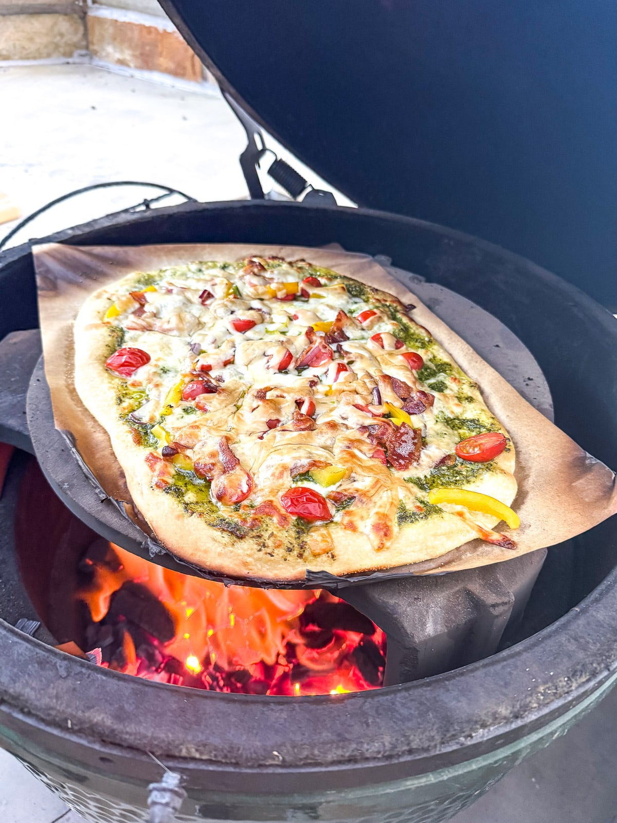 The grill with a pizza on the stone in the Big Green Egg.