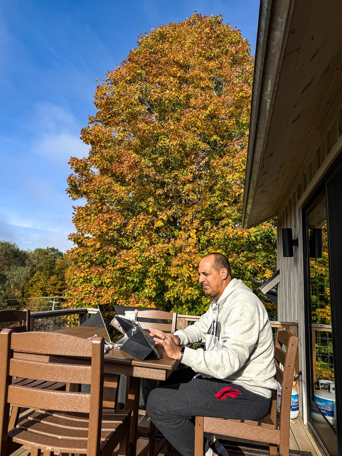 Mike sitting on deck with devices with a beautiful tree in the background.