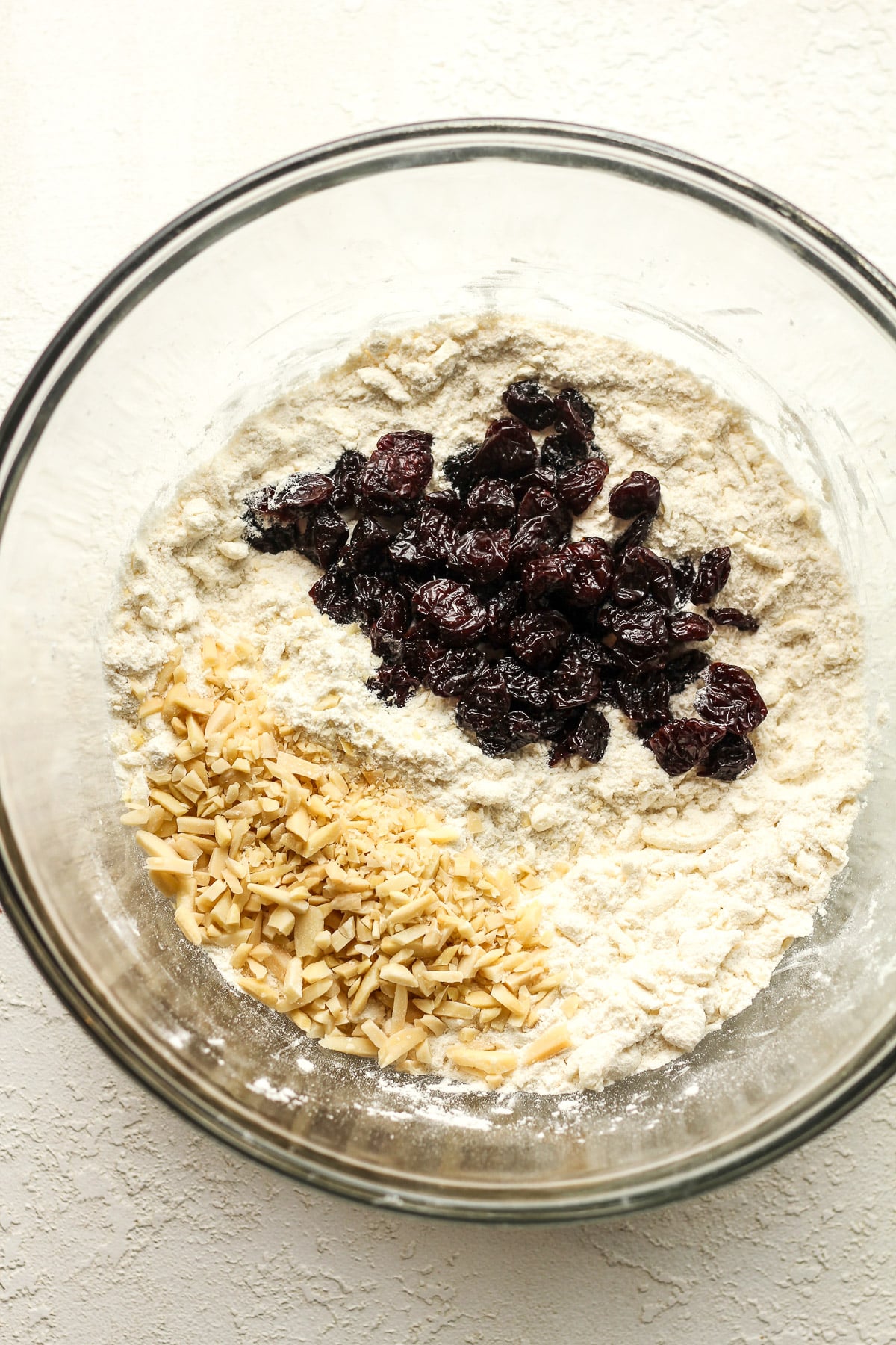 A bowl of the dry ingredients with cherries and almonds on top.
