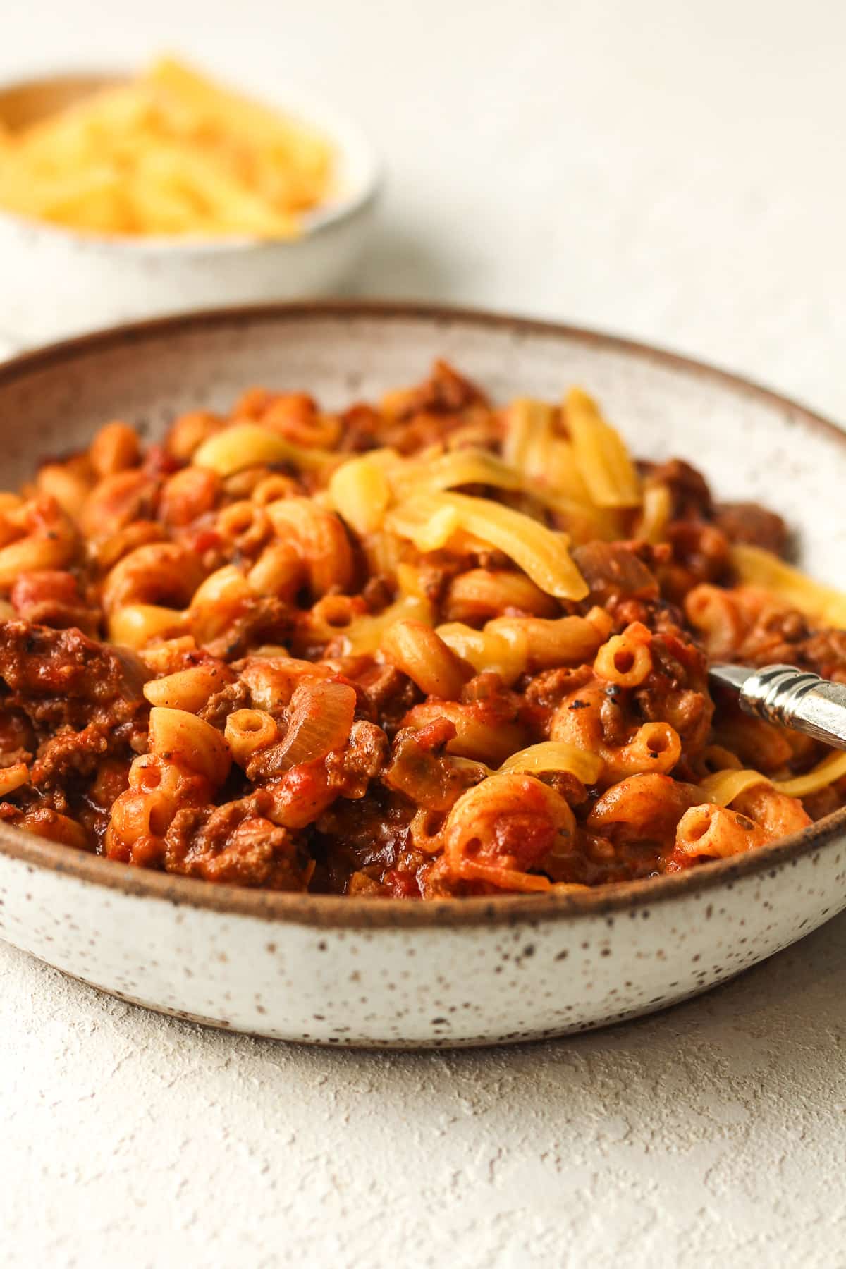 Side view of a bowl of goulash with a small bowl of cheese in the background.