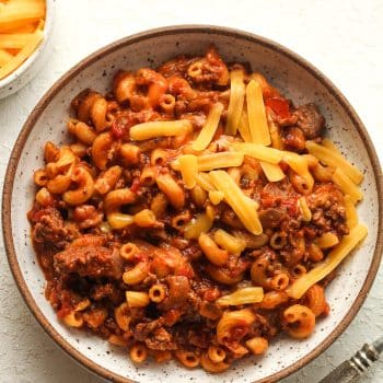 Closeup on a bowl of goulash with shredded cheddar cheese.